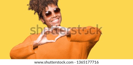 Beautiful young african american woman wearing sunglasses over isolated background smiling in love showing heart symbol and shape with hands. Romantic concept.