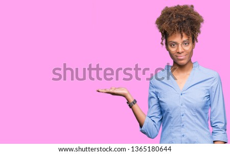 Beautiful young african american business woman over isolated background smiling cheerful presenting and pointing with palm of hand looking at the camera.