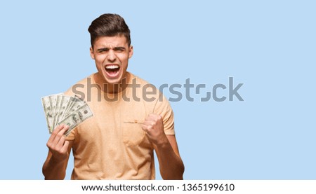 Young man holding dollars screaming very angry and aggressive