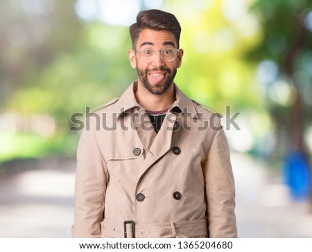 Young man wearing trench coat funnny and friendly showing tongue