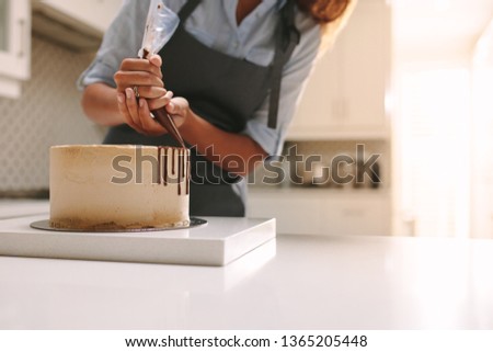 Woman in apron decorating the cake with liquid chocolate. Pastry chef in kitchen decorating cake with chocolate frosting.