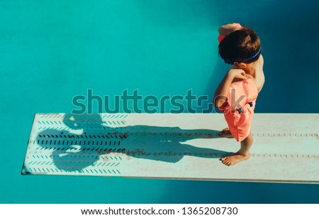 High angle shot of boy with sleeves floats on diving board preparing for dive in the pool. Boy standing on spring board at the swimming pool. Royalty-Free Stock Photo #1365208730