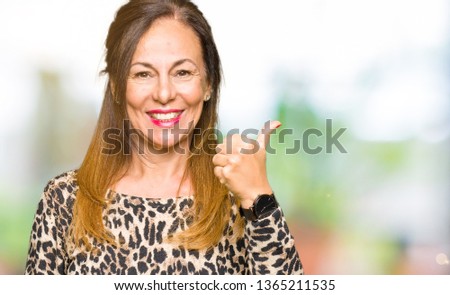 Beautiful middle age woman wearing leopard animal print dress doing happy thumbs up gesture with hand. Approving expression looking at the camera showing success.