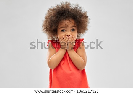 childhood, expression and emotion concept - confused little african american girl covering mouth by hands over grey background