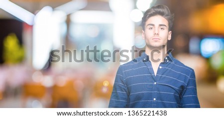 Young handsome man wearing navy shirt over isolated background with serious expression on face. Simple and natural looking at the camera.