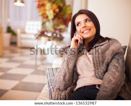 Young happy woman sitting on the sofa at home while talking on phone