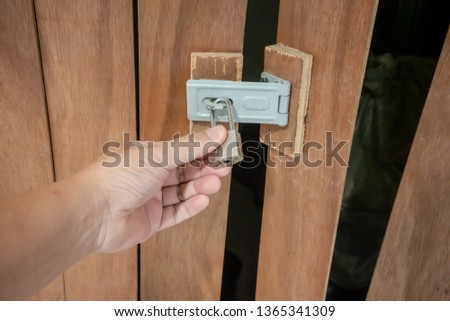 Man hand holding gold locked padlock on wooden door.