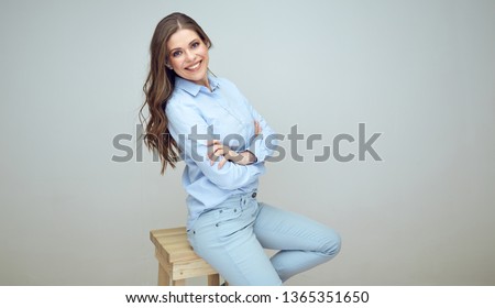 smiling young woman sits on stool with crossed arms. isolated studio portrait.