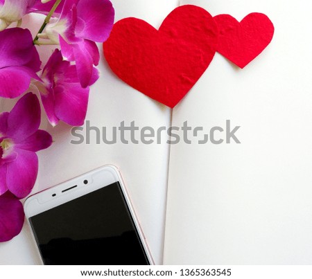 Two red paper hearts, telephone and purple orchid flowers placed on a white Notebook.
Top view with copy space.

