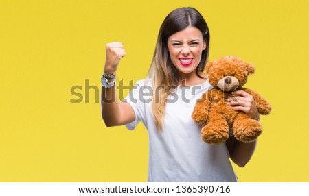 Young beautiful woman holding teddy bear plush over isolated background annoyed and frustrated shouting with anger, crazy and yelling with raised hand, anger concept