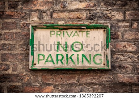 Old wooden "Private No Parking" sign with chipped green paint and rusty nails mounted on a brick wall