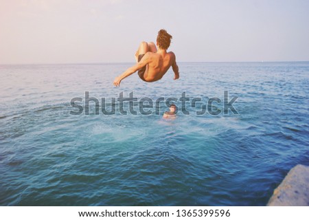 Young man jumping off cliff into blue water ocean at sunset. Active outdoor, holiday adventure, tourism action, healthy summer joy, Fun activity lifestyle. Crazy adult guy in swimwear fly from climb Royalty-Free Stock Photo #1365399596