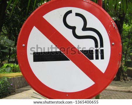 
No smoking sign with white red and black color isolated on trees leaves  grass plant background at the street park. Indicate that the area is forbidden to smoke. Health, eco green concept

