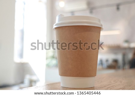 Mock up with a cup of coffee. A glass is on the table in a cafe, selling coffee in the background. Coffee to go. Light walls. Wooden table. Cafe. Flowers