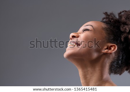 Happy vivacious laughing young African woman tilting her head back with a joyful smile in a close up cropped portrait on grey with copy space