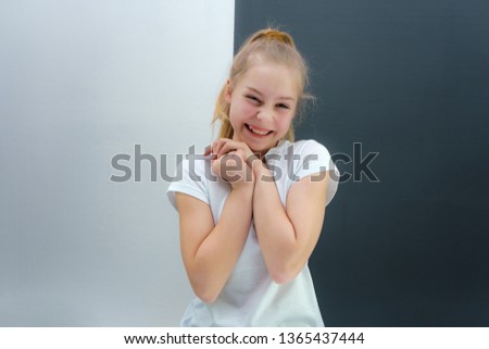 A concept portrait of a cute pretty blonde teen girl with long hair is sitting in a white T-shirt against a gray-white background and talking. She's right in front of the camera.