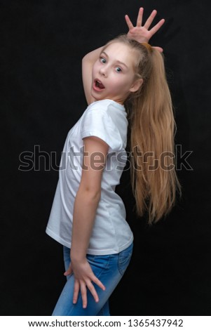 Concept portrait of a cute pretty blonde teen girl with long hair posing in white t-shirt on black background in studio. She's right in front of the camera.