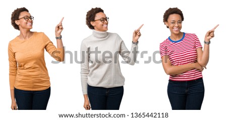 Young african american woman with afro hair wearing glasses with a big smile on face, pointing with hand and finger to the side looking at the camera.