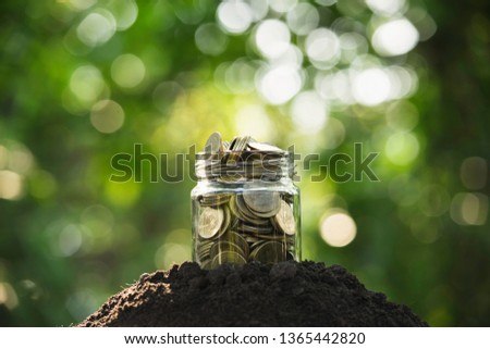 Coins in glass jar putting on soil in nature for save concept.