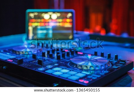 Professional disc jockey midi controller device and notebook with audio mixing software on festival stage in nightclub.Dj turntable player in bright neon blue lights on scene in music hall