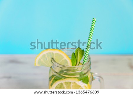Mason jar glass of homemade lemonade with lemons, mint and paper straw on turquoise background. Summer refreshing beverage.