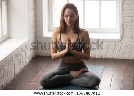 Beautiful woman practicing yoga, sitting in Lotus pose with namaste, Padmasana exercise, attractive girl in grey sportswear, leggings and bra working out at home or in yoga studio vertical photo