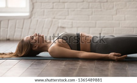 Beautiful woman with closed eyes practicing yoga, lying in Savasana, Dead Body pose on mat, attractive girl in grey sportswear, pants and bra working out at home or in yoga studio, close up Royalty-Free Stock Photo #1365489881