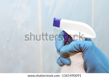 Cleaning the tile from the sprayer with the product in blue rubber gloves on the tile visible foam from the tool