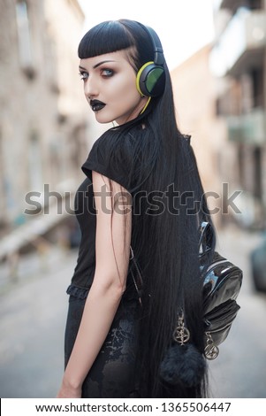 Urban goth girl listening to her favourite music over her big headphones, street in a city surroundings Royalty-Free Stock Photo #1365506447