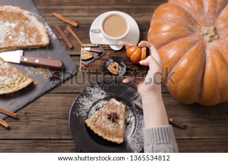 girl takes  picture of  pumpkin pie on  mobile phone on old wooden background