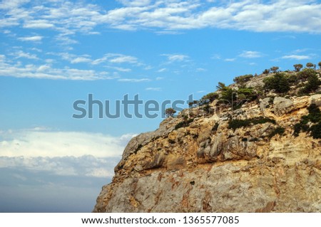 Steep rock with trees against a blue sky.