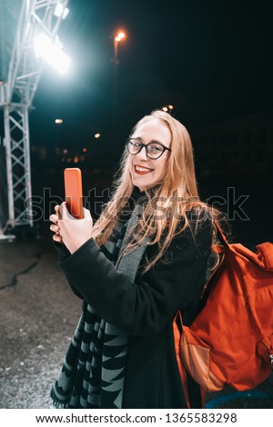 Blonde woman with smartphone at night in the street.