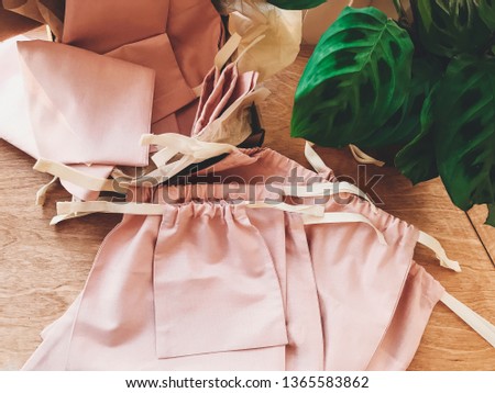 Eco friendly linen bags on wooden background with green leaves plant, flat lay. Zero waste shopping concept. Ban single use plastic . Reusable eco bags for groceries.