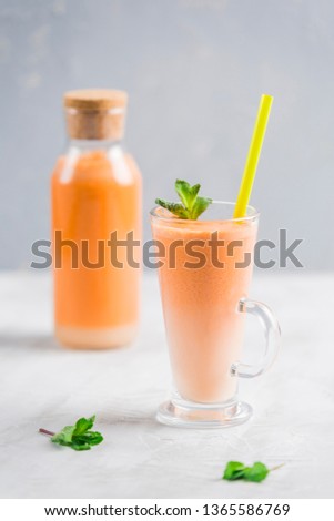 Fresh carrot juice with oat milk and mint. Vegetarian drink for healthy food in a transparent glass on a light background side view.
