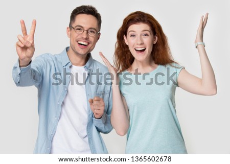 Happy young couple stand isolated on grey studio background feel excited winning lottery, smiling millennial man and woman laughing have fun gesturing, celebrating or posing for picture