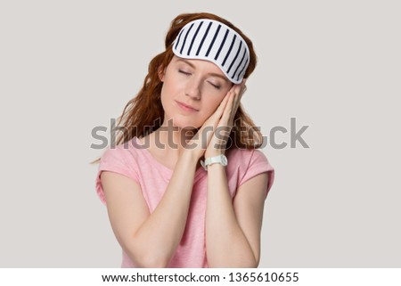 Calm tired red-haired girl with sleeping mask on head stand asleep relax on hands, exhausted relaxed redhead woman isolated on grey studio background sleep feel cozy in comfortable homewear