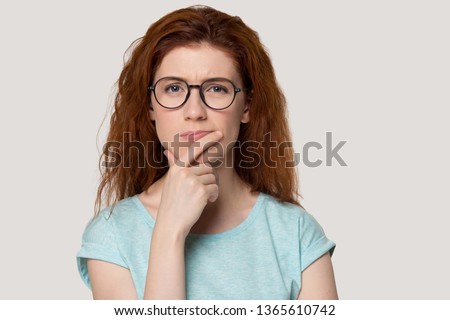 Pensive young red-haired young woman isolated on grey background look at camera thinking, thoughtful redhead girl in glasses pondering planning problem solution, lost in thoughts consider idea Royalty-Free Stock Photo #1365610742