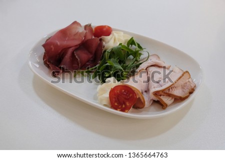 Cutting meat and ham on a white plate and some greens. Food photography.