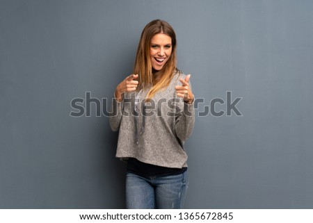 Blonde woman over grey background points finger at you while smiling