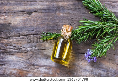 Top view Bottle glass of essential rosemary oil with rosemary branch and flower on wooden rustic background. herbal oil concept  Royalty-Free Stock Photo #1365704798