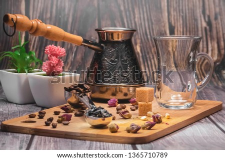 Measuring spoon for tea and coffee with coffee beans and dry tea leaves wth glass tea cup and copper cezve with orange wooden handle for Turkish coffee on a wooden plate. Jasmine, small roses, coffee