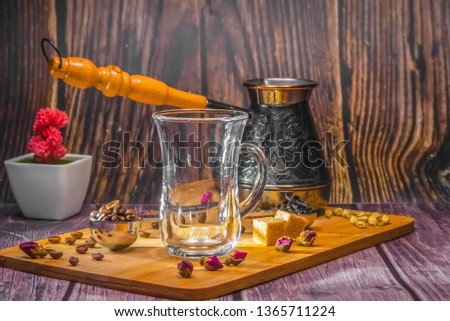 Measuring spoon for tea and coffee with coffee beans and dry tea leaves wth glass tea cup and copper cezve with orange wooden handle for Turkish coffee on a wooden plate. Jasmine, small roses, coffee. 
