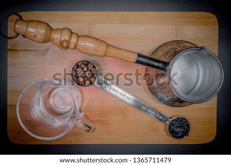 Measuring spoon for tea and coffee with coffee beans and dry tea leaves wth glass tea cup and copper cezve with orange wooden handle for Turkish coffee. Grey background. Indoor. Lamps light.