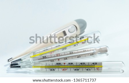 Digital and 3 mercury medical thermometers on neutral background. Indoor. Lamp lights. Closeup. Macro.