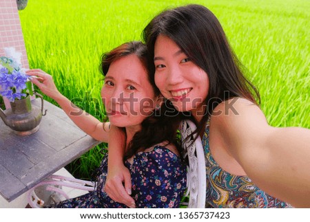 young happy and pretty Asian Chinese girl taking selfie photo outdoors with her mother, a 60s mature woman , enjoying Summer holidays travel together at beautiful tropical destination