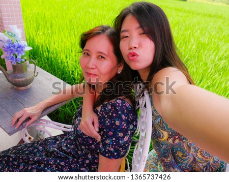 young happy and pretty Asian Chinese girl taking selfie photo outdoors with her mother, a 60s mature woman , enjoying Summer holidays travel together at beautiful tropical destination