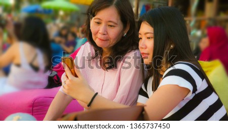 young happy and pretty Asian Chinese girl on the beach taking selfie photo with her mother, a 60s mature woman , enjoying Summer holidays travel together at beautiful tropical destination