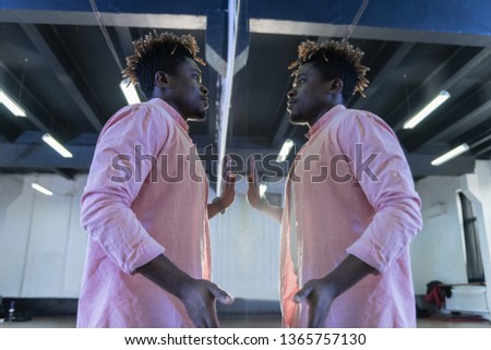 Time in studio. Appealing concentrated young man looking on himself in mirror and touching it with hands