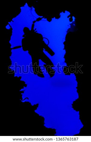A silhouette shot of a scuba diver with an underwater camera in his hand descending into the abyss. The image is framed by a naturally occuring hole in the reef