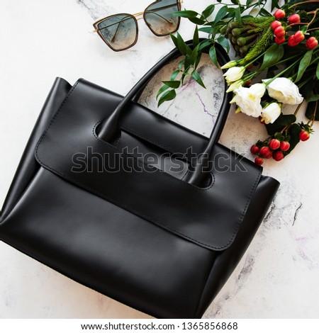 Black leather bag and flowers on a grey concrete background